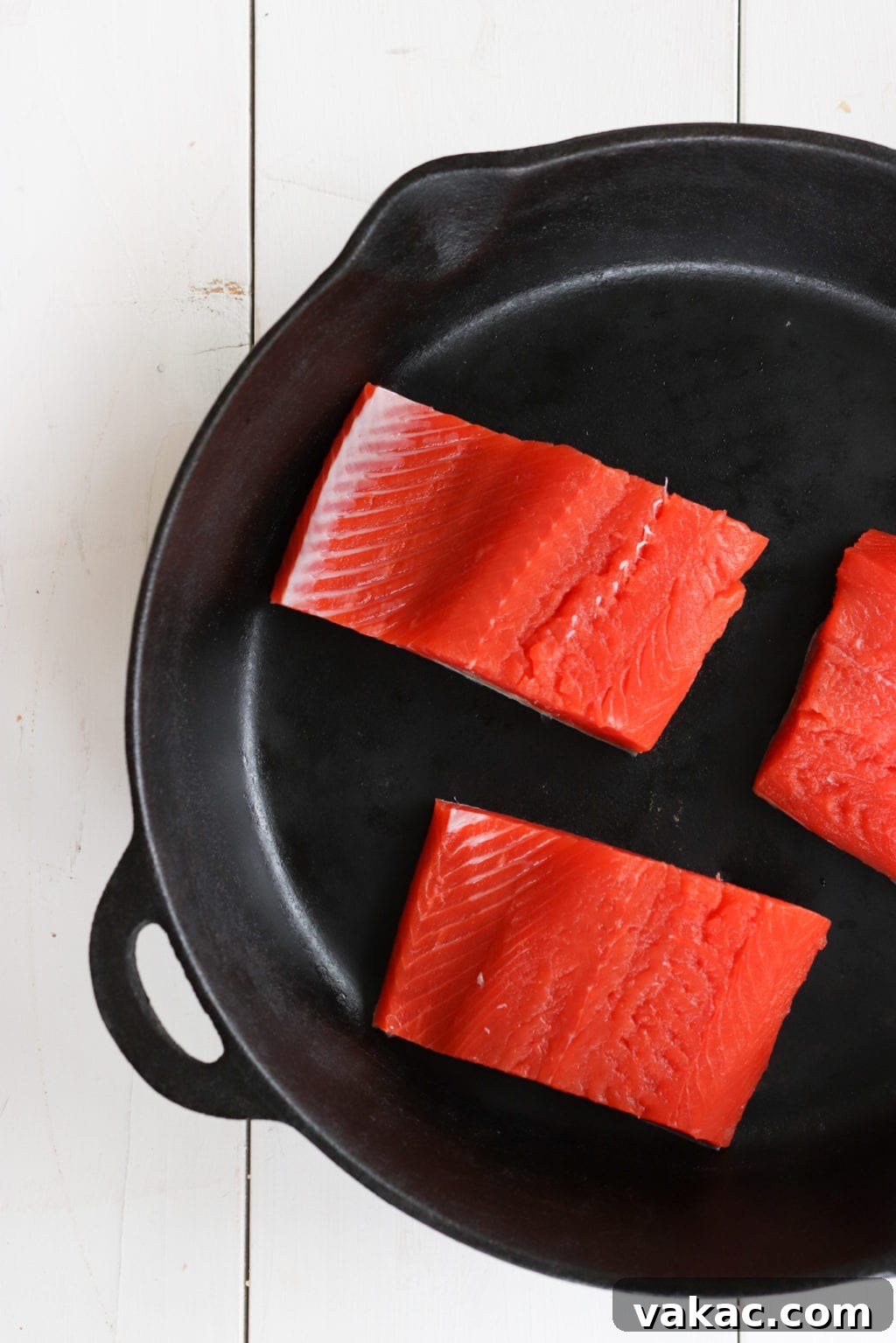 Oven-baked Miso Yogurt Salmon Recipe by Lindsay Pleskot, Dietitian Fresh, vibrant salmon fillets arranged neatly on a cast iron skillet, ready to be seasoned and marinated. The clean, simple presentation emphasizes the quality of the ingredients, perfect for a healthy and easy meal preparation.