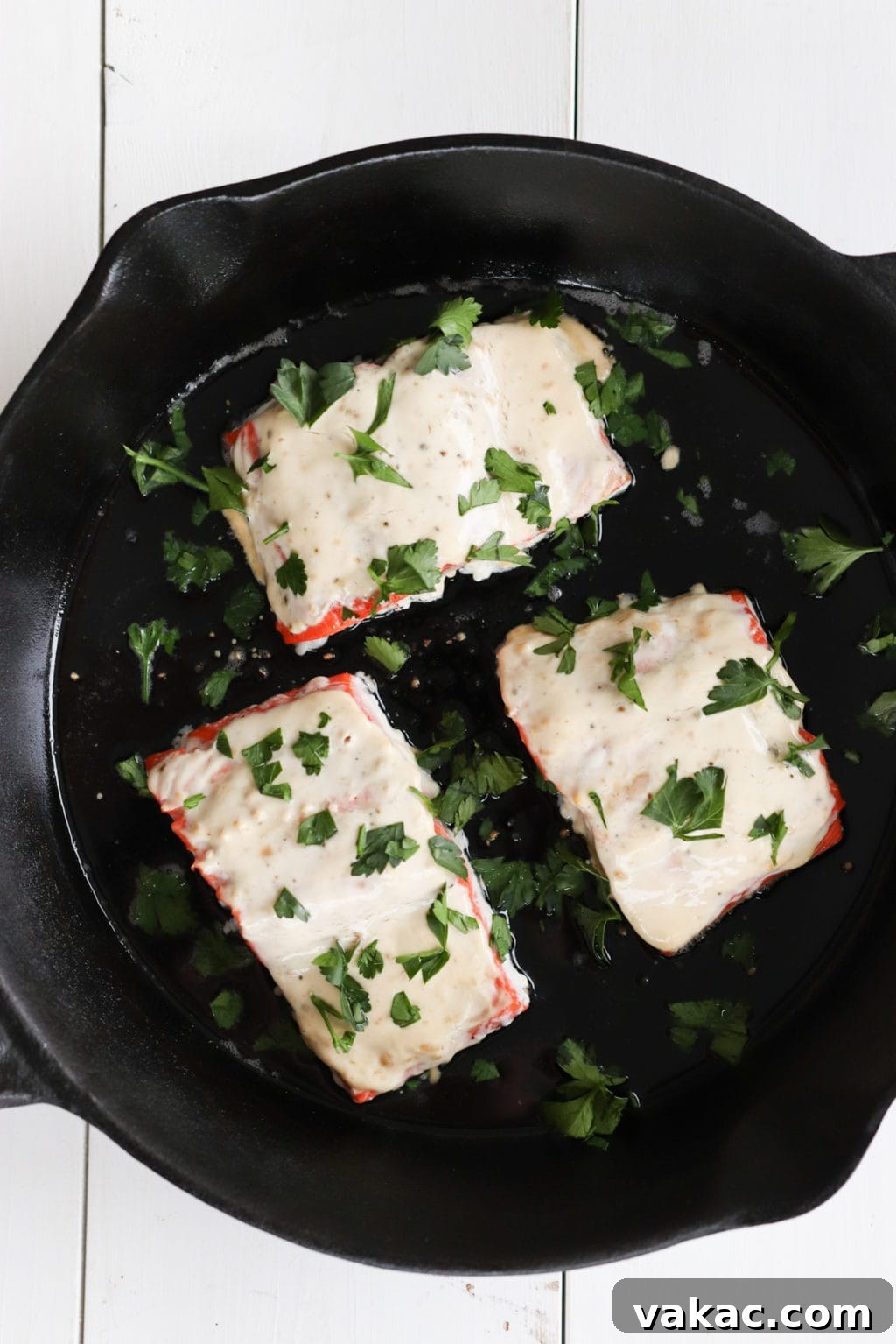 Oven-baked Miso Yogurt Salmon Recipe by Lindsay Pleskot, Dietitian A vibrant close-up of Miso Oven-Baked Salmon in a sizzling cast iron skillet, fresh out of the oven. The salmon fillets are generously coated with a rich, creamy sauce and beautifully caramelized, highlighting the delicious textures and golden hues of the dish.