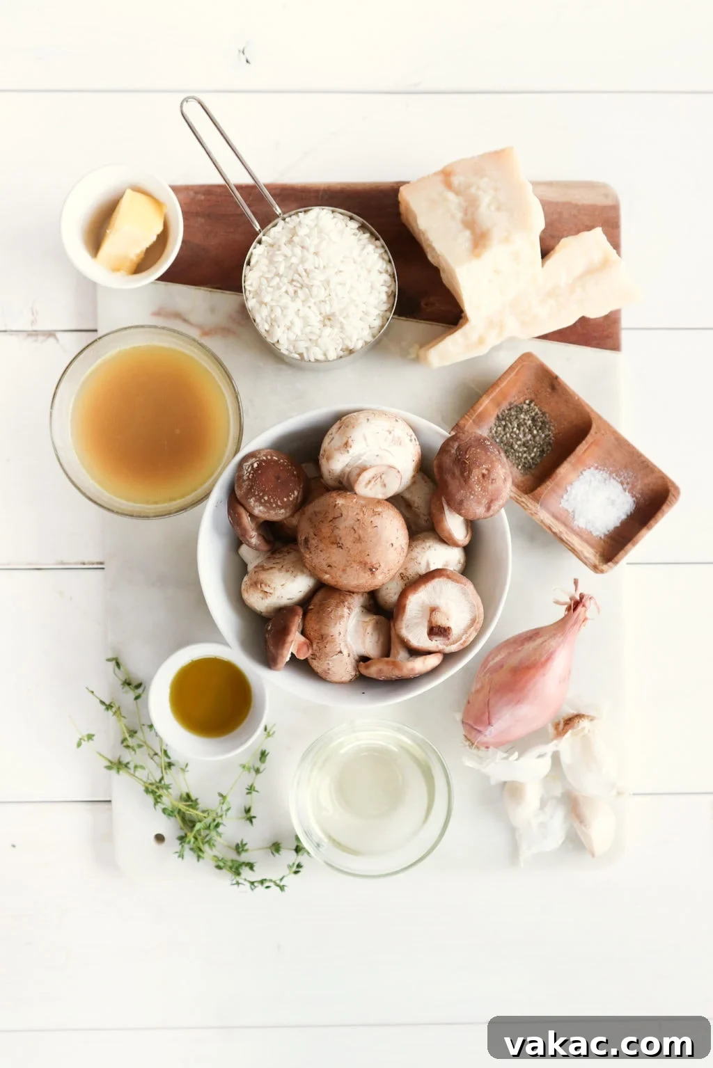 A cutting board over a white food photography board with creamy mushroom risotto ingredients: butter, rice, Parmesan, vegetable stock, mushrooms, salt and pepper, onion, garlic.
