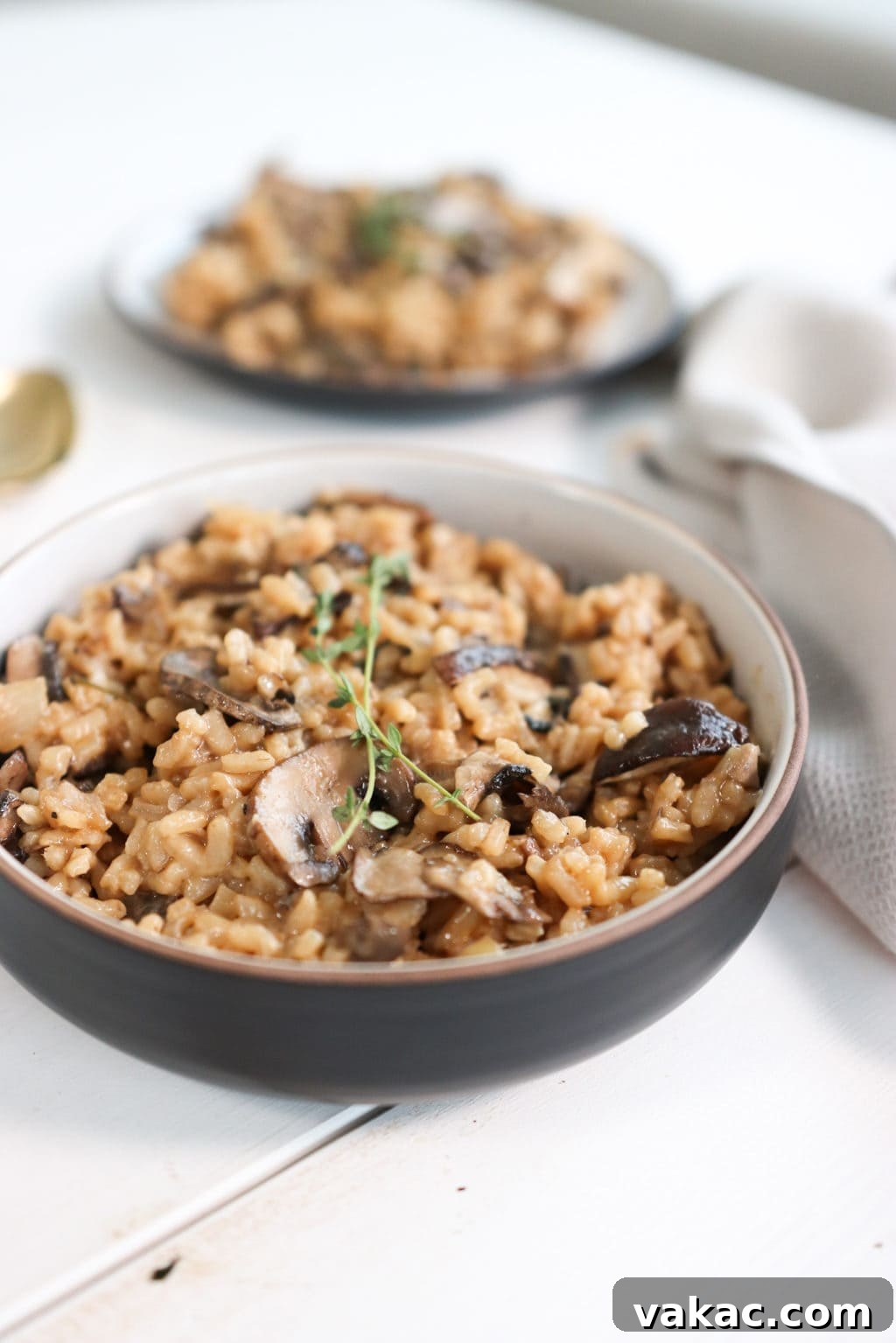 Creamy mushroom risotto in a white and brown bowl over a white food board. Ingredients include: mushrooms, garlic, parsley, arborio rice, white wine, vegetable stock, parmesan, butter