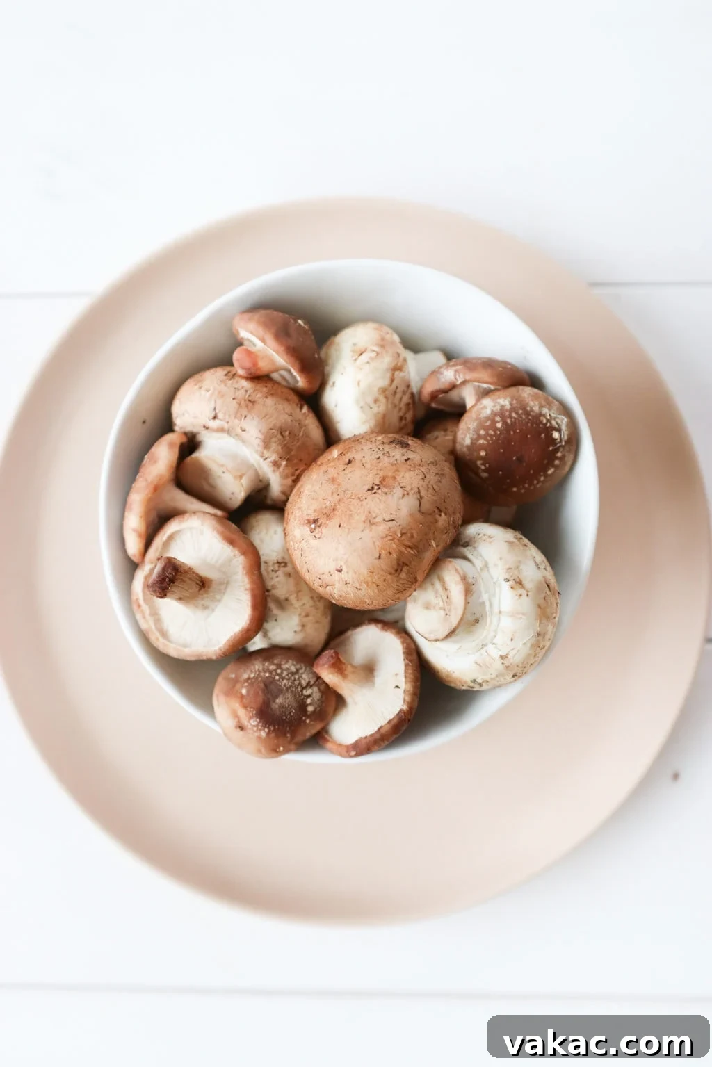 A pink plate over a white food photography board with a white bowl of mushrooms.