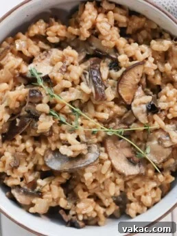 Creamy mushroom risotto in a white bowl over a white food board. Ingredients include: mushrooms, garlic, parsley, arborio rice, white wine, vegetable stock, parmesan, butter