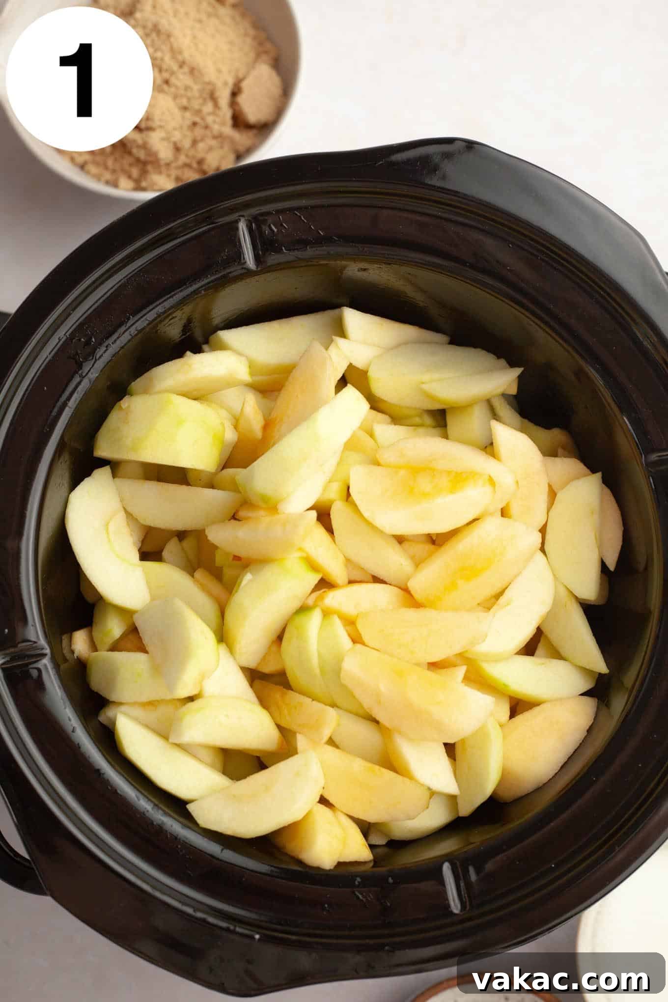 Classic Homemade Apple Butter Recipe 4 An overhead shot of neatly sliced apples layered within the basin of a slow cooker, ready for cooking.