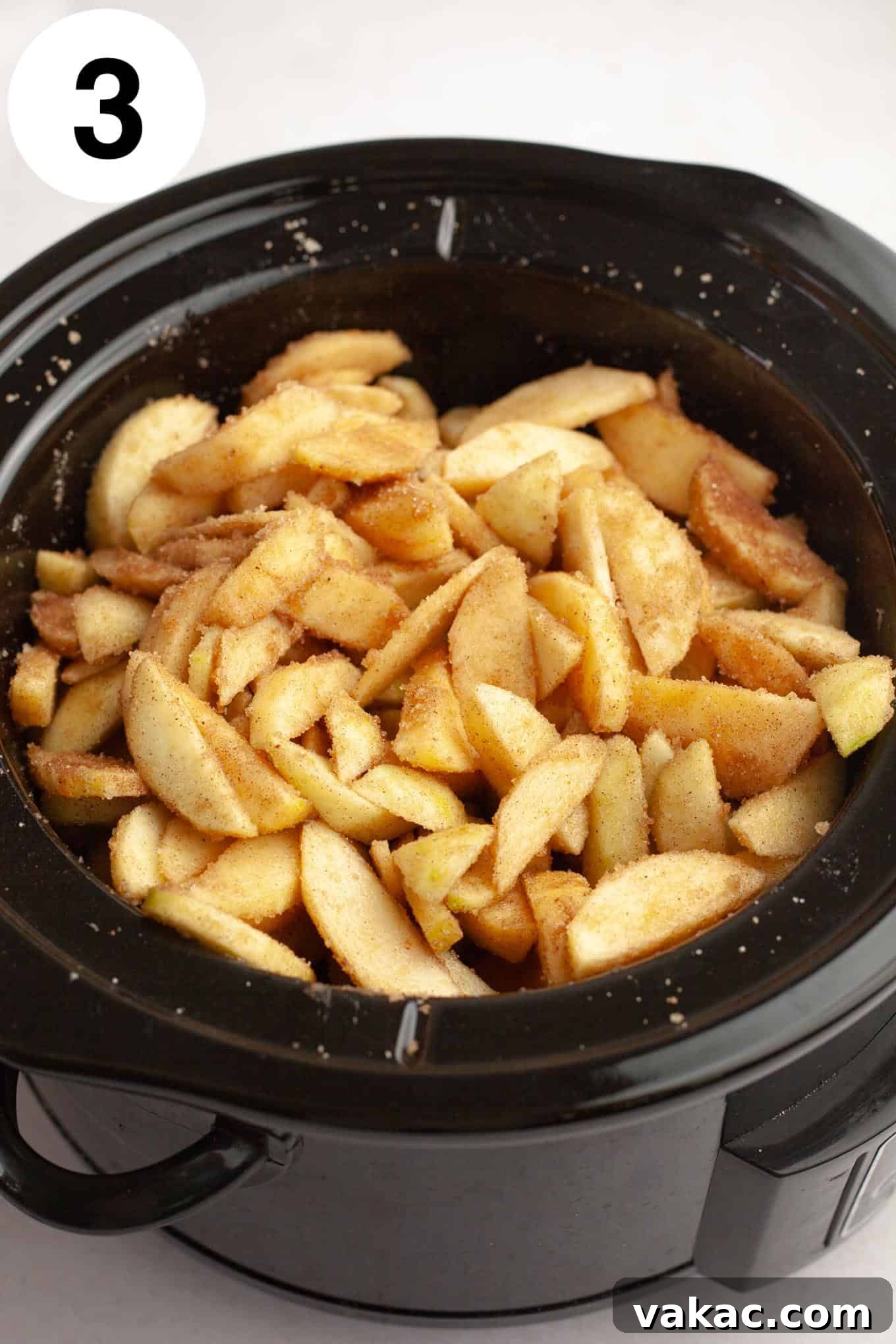 Classic Homemade Apple Butter Recipe 6 An overhead view of sliced apples in a slow cooker, now generously coated with the mixed sugar and spice blend.