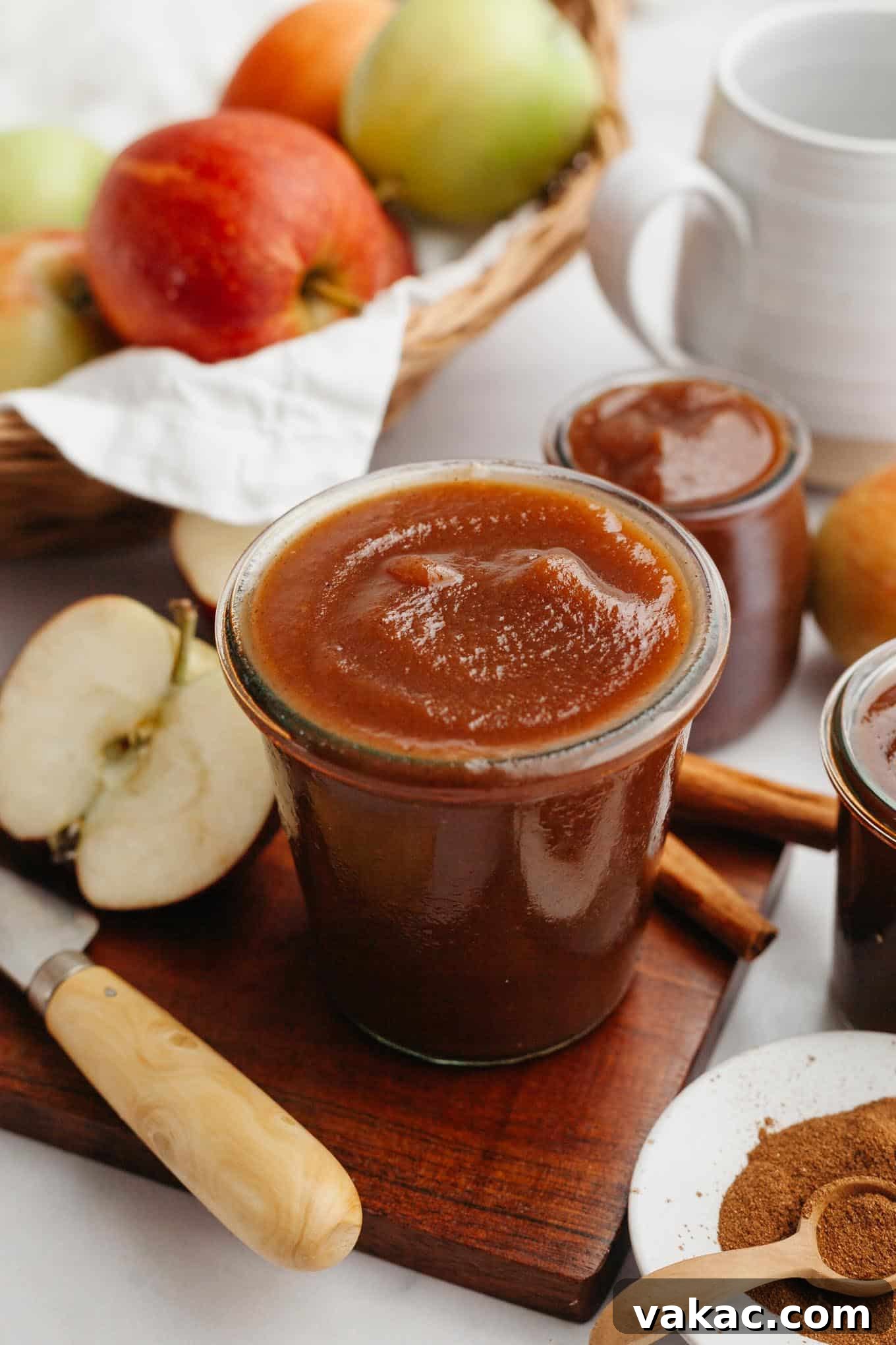 Classic Homemade Apple Butter Recipe 10 A rustic scene featuring a jar of apple butter on a wooden cutting board, surrounded by fresh apples, cinnamon sticks, and scattered whole spices.