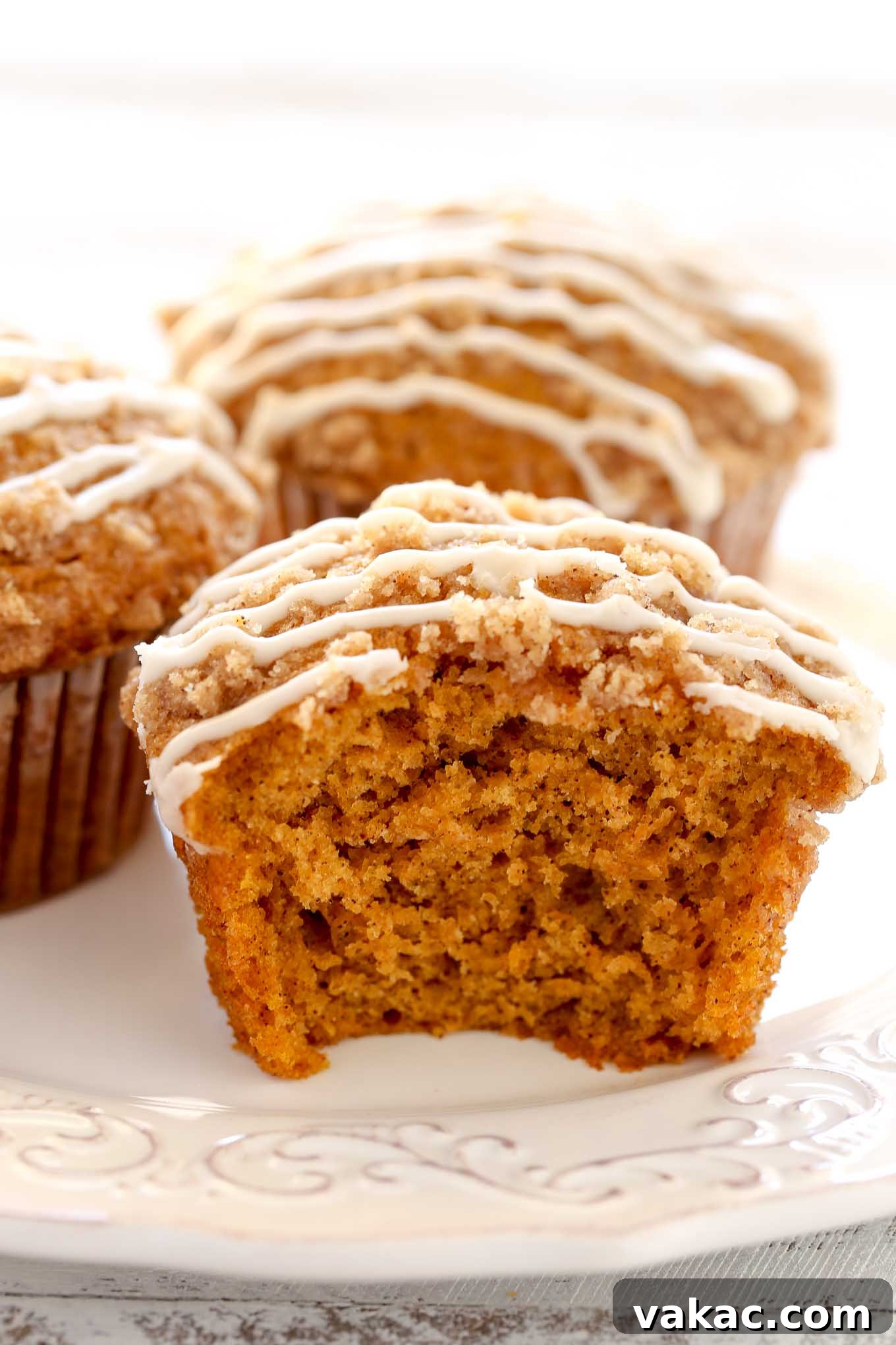 Close up view of pumpkin muffins on a white plate. The front muffin has a bite missing. 