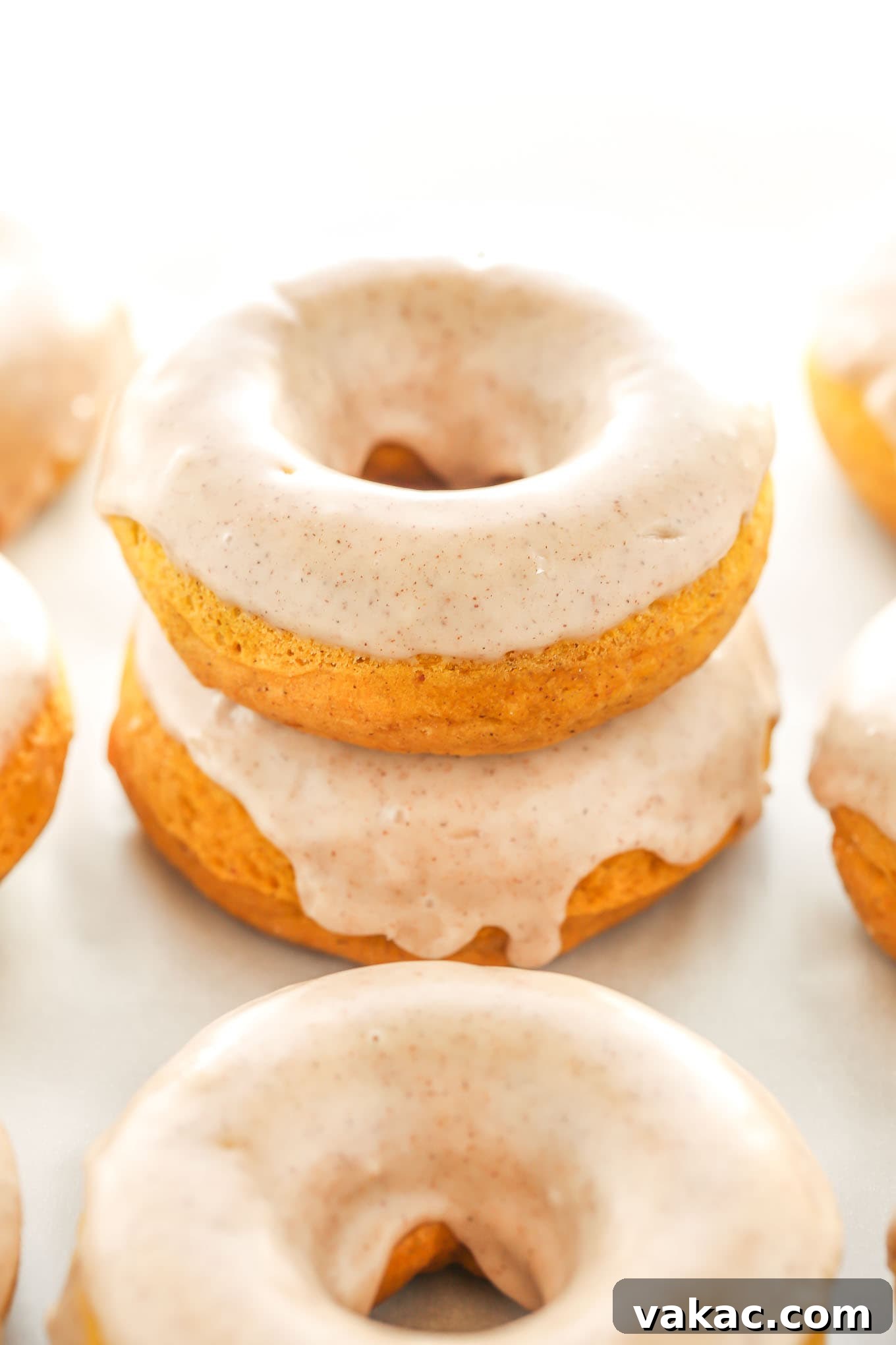 Cozy Autumn Pumpkin Doughnuts with Maple Cinnamon Drizzle 2 A stack of two perfectly baked pumpkin donuts, glistening with maple cinnamon glaze. Several other donuts are artfully arranged around them on a rustic wooden surface, suggesting a bountiful fall treat.