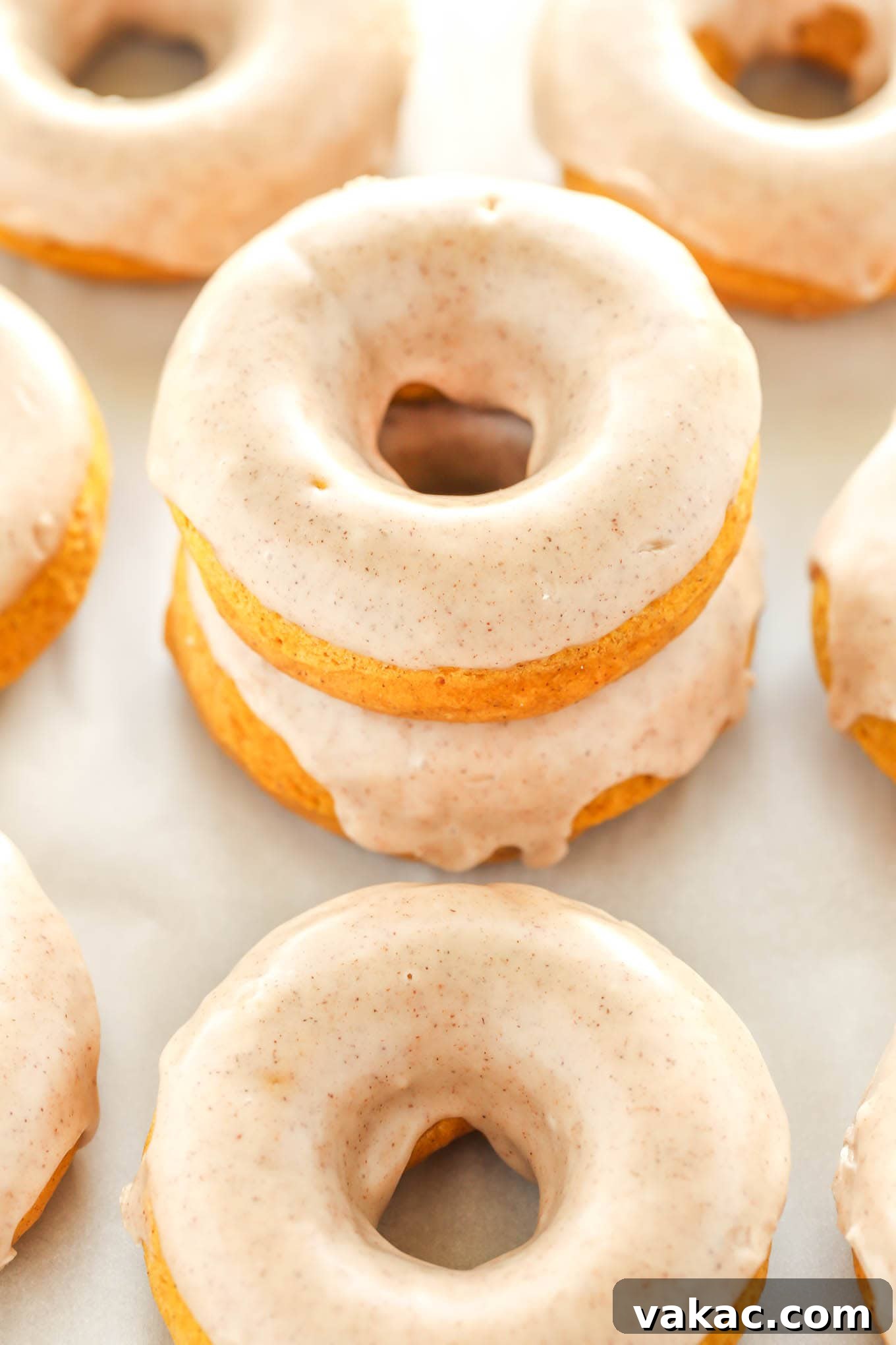 Cozy Autumn Pumpkin Doughnuts with Maple Cinnamon Drizzle 4 A perfectly arranged stack of two baked pumpkin donuts, with additional glazed donuts scattered around them on a pristine white surface, highlighting their tempting texture and warm color.