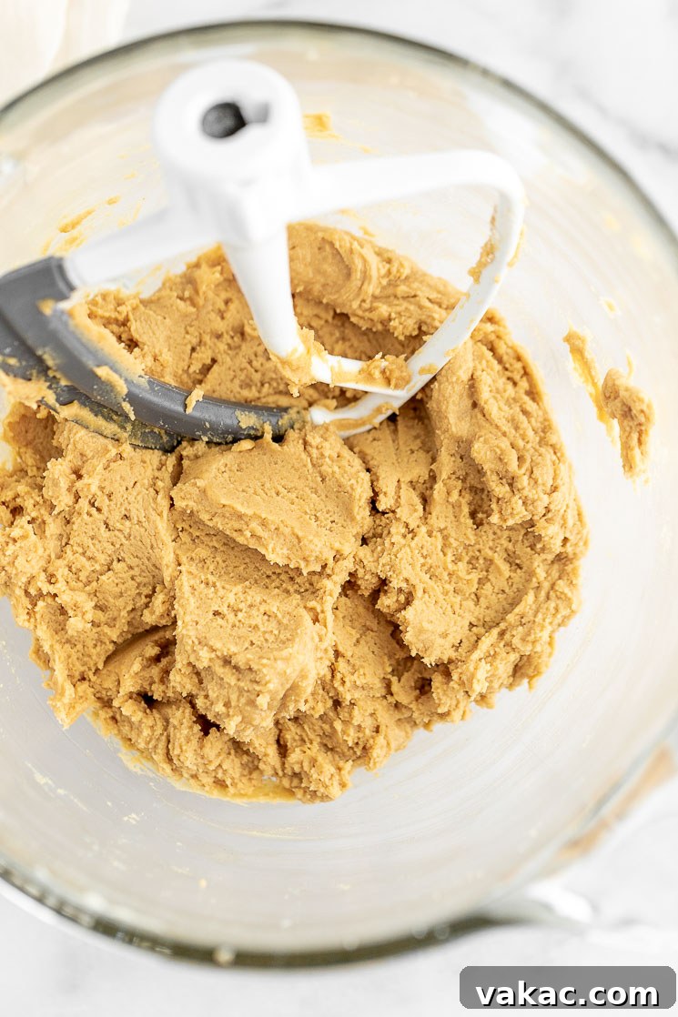 A glass mixing bowl with peanut butter cookie dough with the beater still in it.