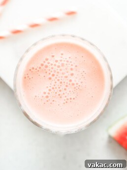 A glass of watermelon banana smoothie with a pink and white straw, garnished with watermelon slices.