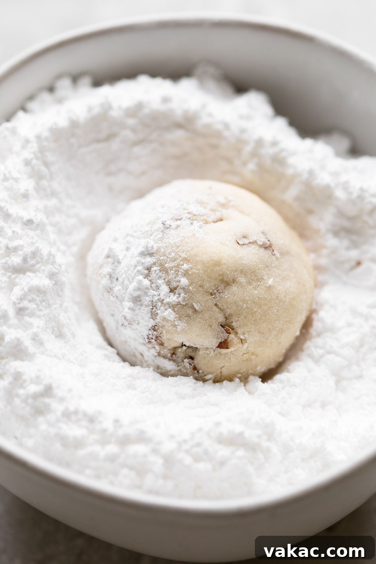 Powdered Perfection: Snowball Cookies 6 A baked snowball cookie being rolled in powered sugar before being set aside to cool completely.