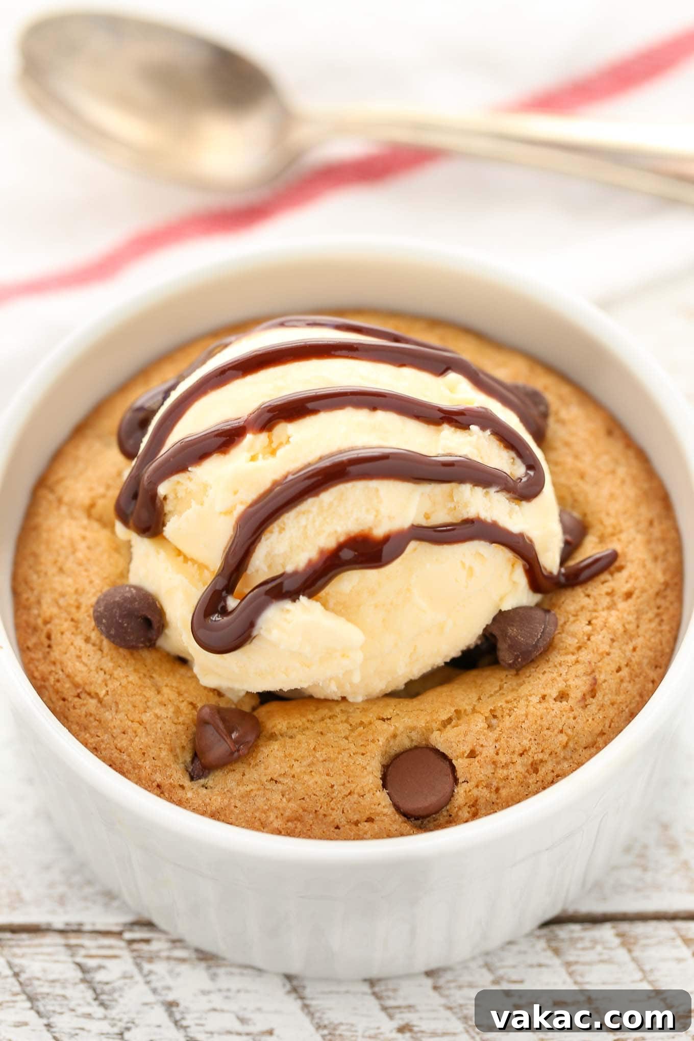 Close up of a deep dish chocolate chip cookie topped with vanilla ice cream and chocolate sauce.