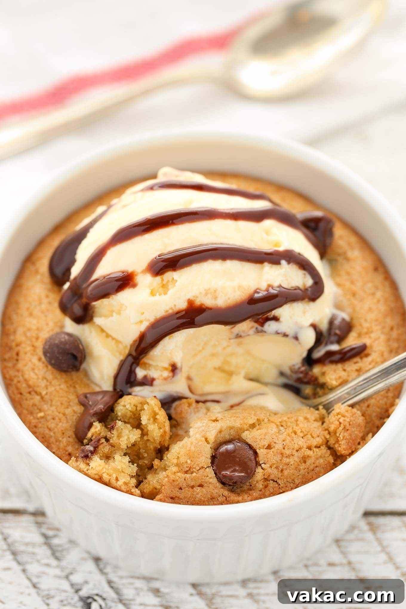 A deep dish single serve chocolate chip cookie topped with ice cream and chocolate sauce. A spoon is being dug into the cookie.