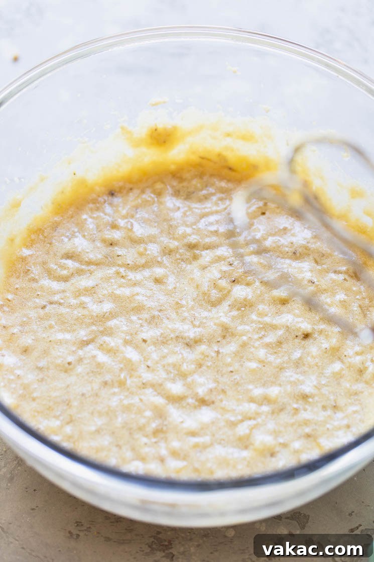 A glass bowl filled with the wet ingredients for banana bread, mixed until smooth and creamy.