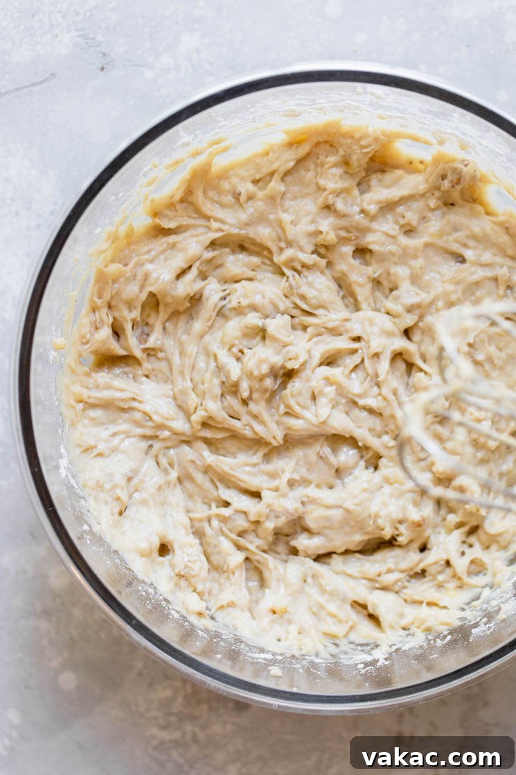A glass bowl containing the finished banana bread batter, thick and ready to be poured into a loaf pan for baking.