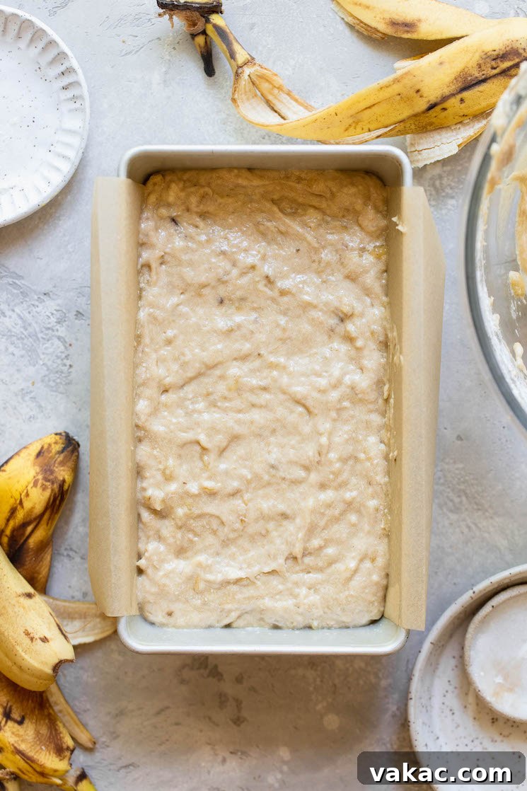 Perfectly Moist Banana Bread 6 A loaf pan lined with parchment paper, filled with banana bread batter, ready to be placed into the oven.