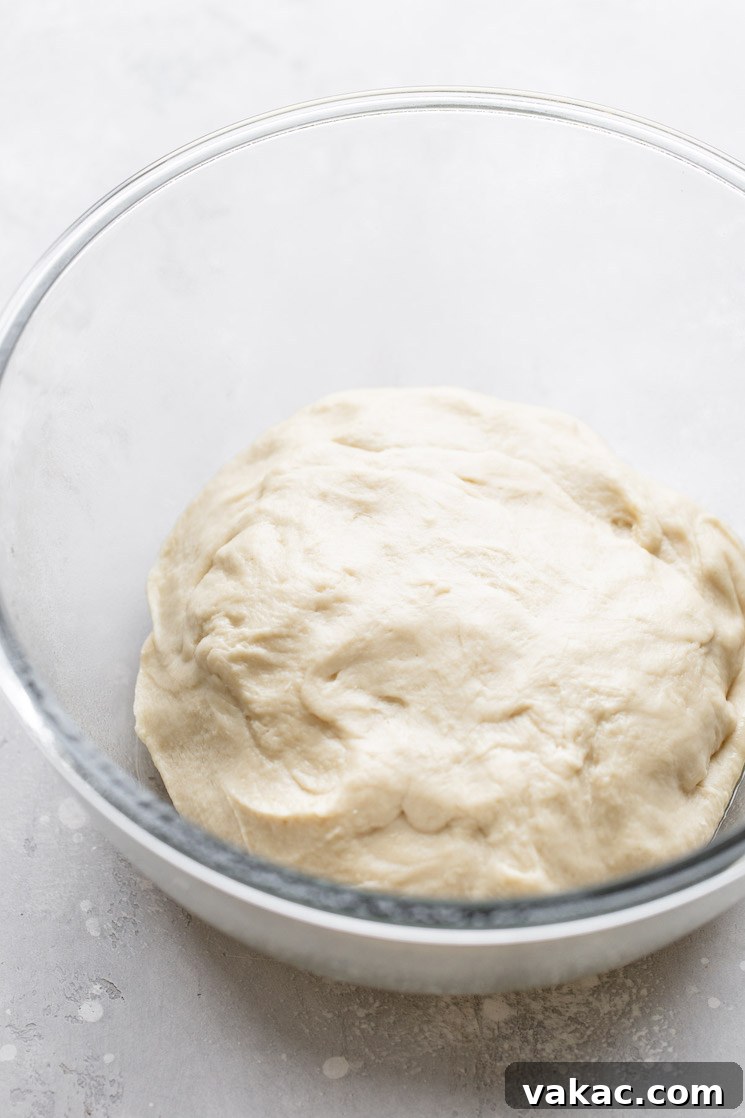 A glass mixing bowl holding the finished cinnamon roll dough that needs to rise.