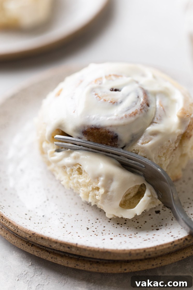 Grandmas Legendary Cinnamon Swirls 8 A single cinnamon roll on a white speckled plate being cut into with a fork, showing its gooey center.