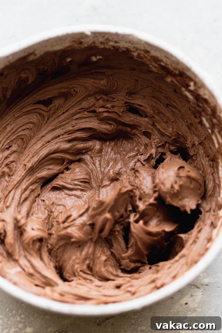 The Ultimate Chocolate Chip Cookie Cake 6 A white mixing bowl filled with chocolate buttercream frosting, perfectly whipped and ready to be used.