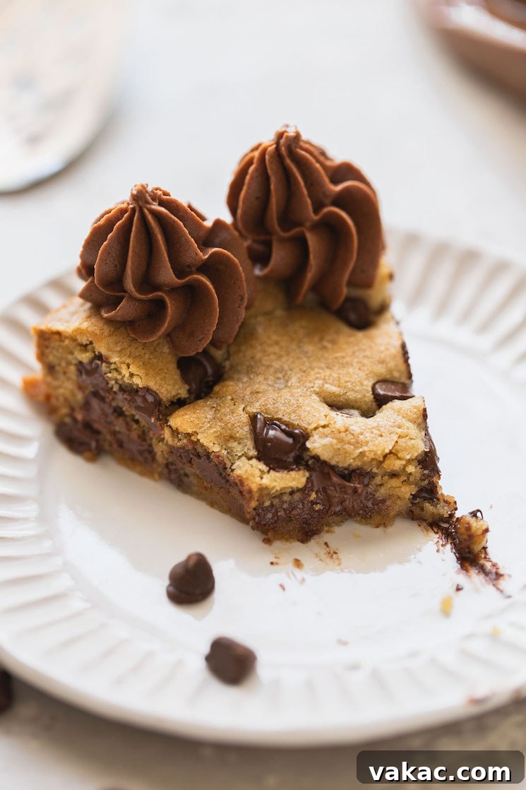 The Ultimate Chocolate Chip Cookie Cake 8 A single piece of cookie cake with a bite taken out of it on a white plate, showing the soft texture.
