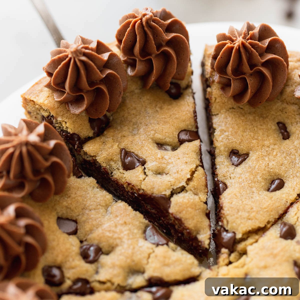 The Ultimate Chocolate Chip Cookie Cake 9 A cookie caked sitting on a white cake stand with a sliced being taken out of it.