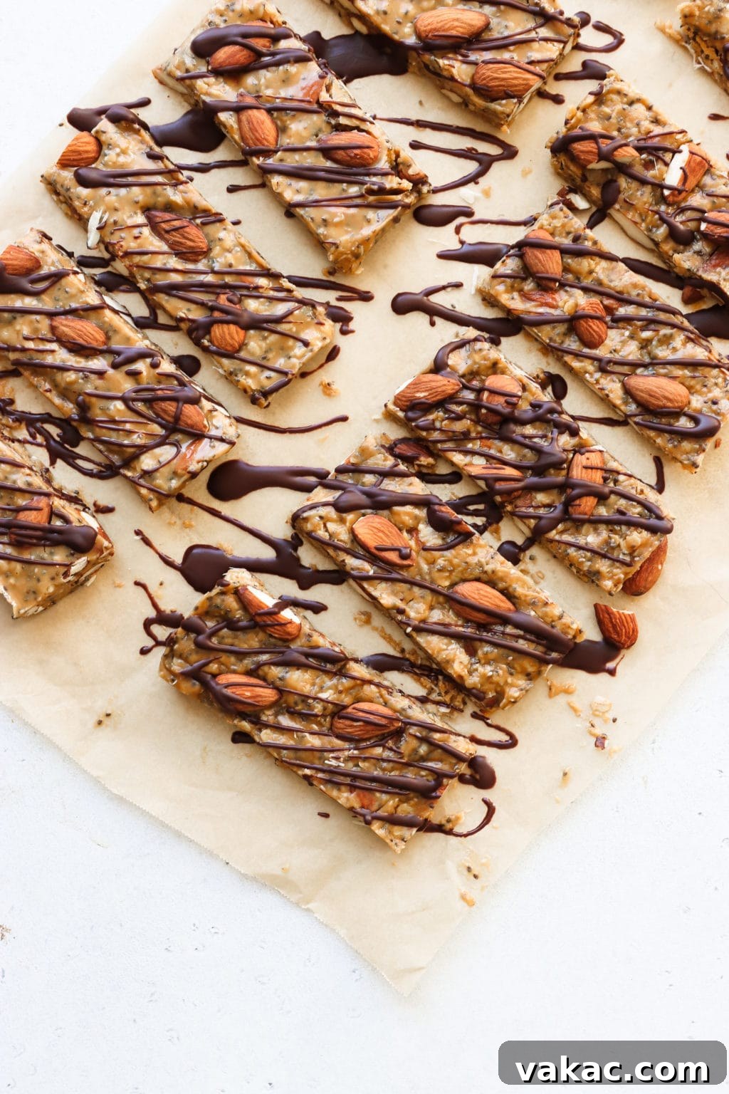Effortless Granola Energy Bars 2 9 no-bake granola bars topped with almonds and chocolate drizzle are on a piece if parchment paper