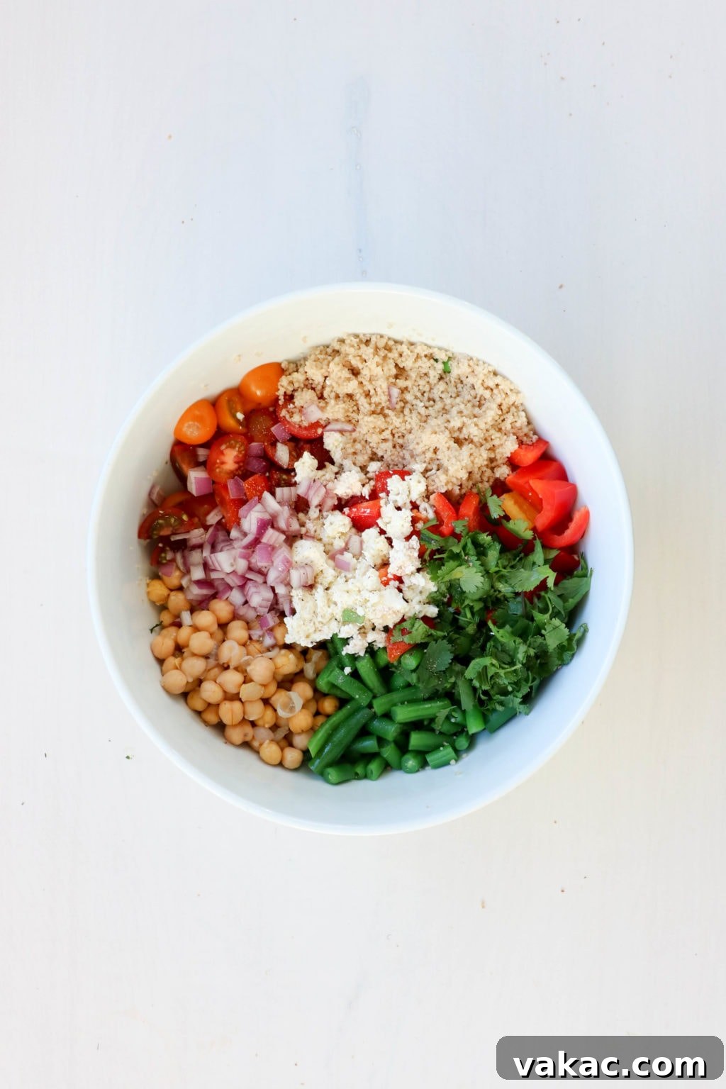 A bowl of quinoa, tomatoes, chickpeas, feta, green beans, red onions and red peppers in a bowl.