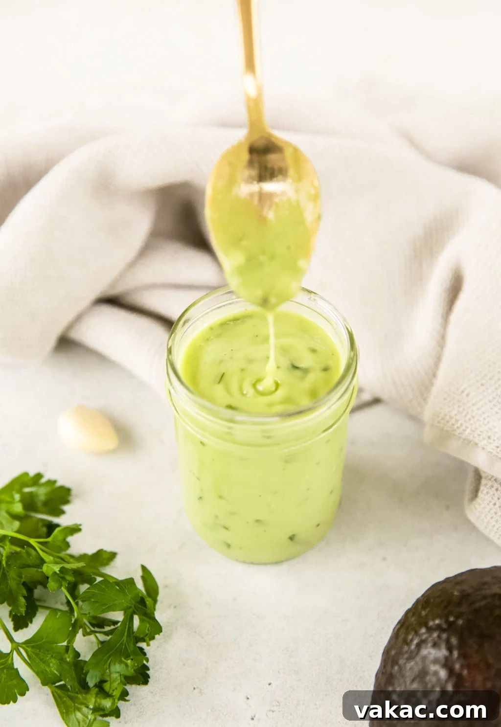 Avocado green goddess dressing dripping from a gold spoon into a full mason jar of the dressing
