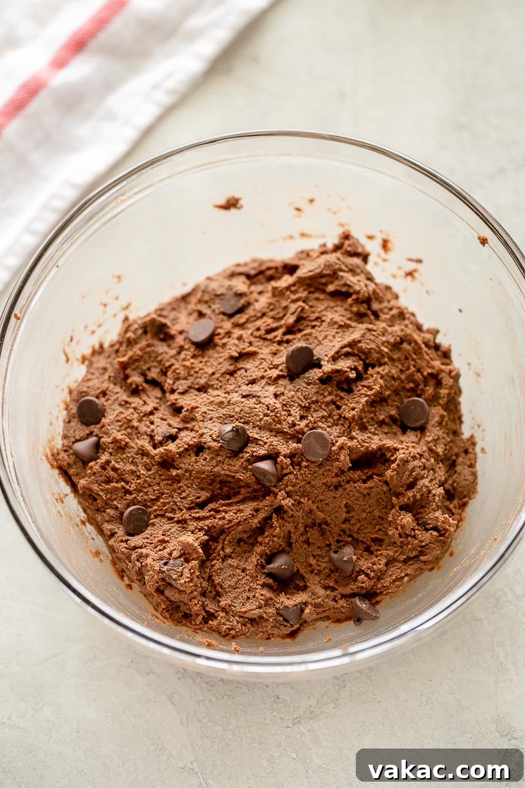 A glass bowl filled with rich, dark double chocolate chip cookie dough, studded with chocolate chips, ready for chilling.