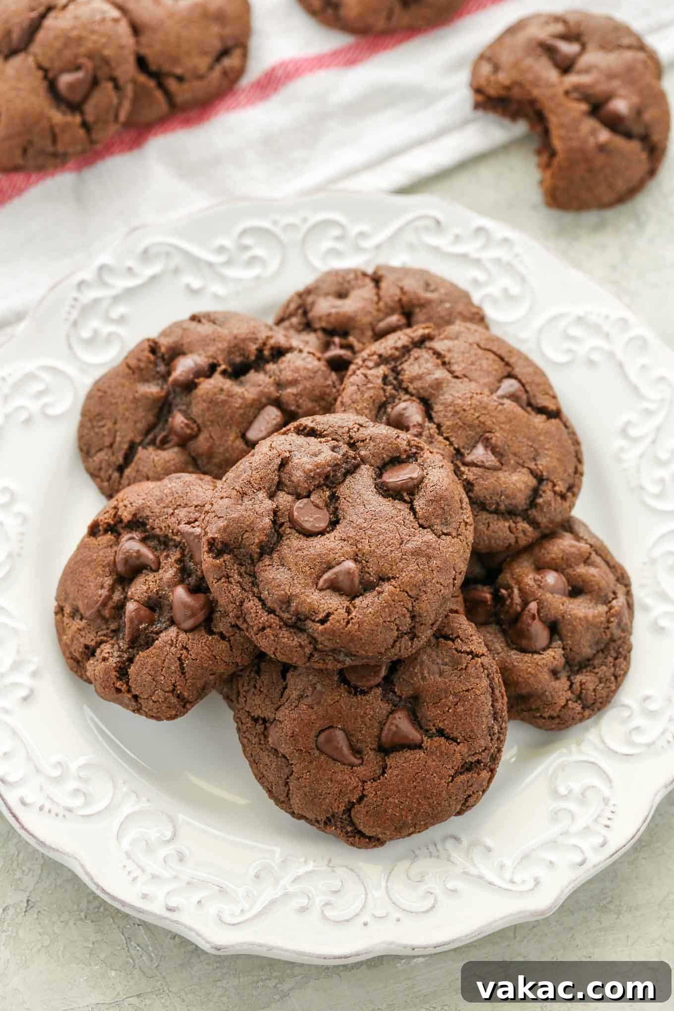 Decadent Double Chocolate Delights 7 A white plate filled with chocolate cookies, with more cookies casually scattered around it on a patterned surface, highlighting their visual appeal.