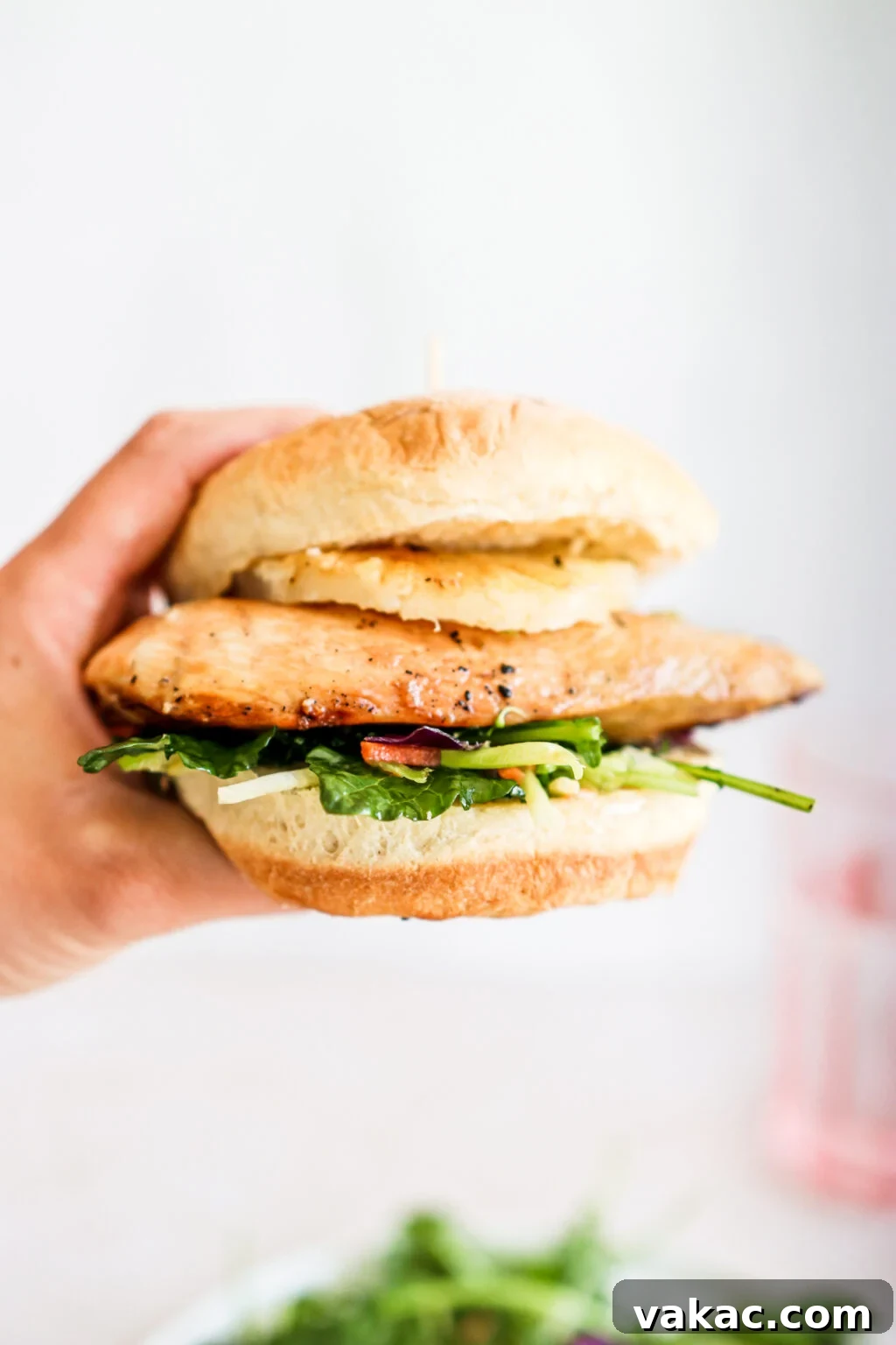Sweet & Umami Maple-Soy Chicken Burger 10 A hand is holding up a grilled chicken burger with a pineapple ring, slaw and spinach.