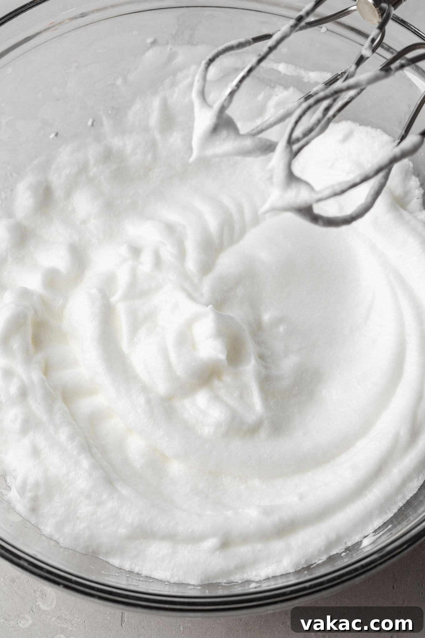 A close-up shot of stiff egg whites in a clear glass mixing bowl, demonstrating proper aeration.