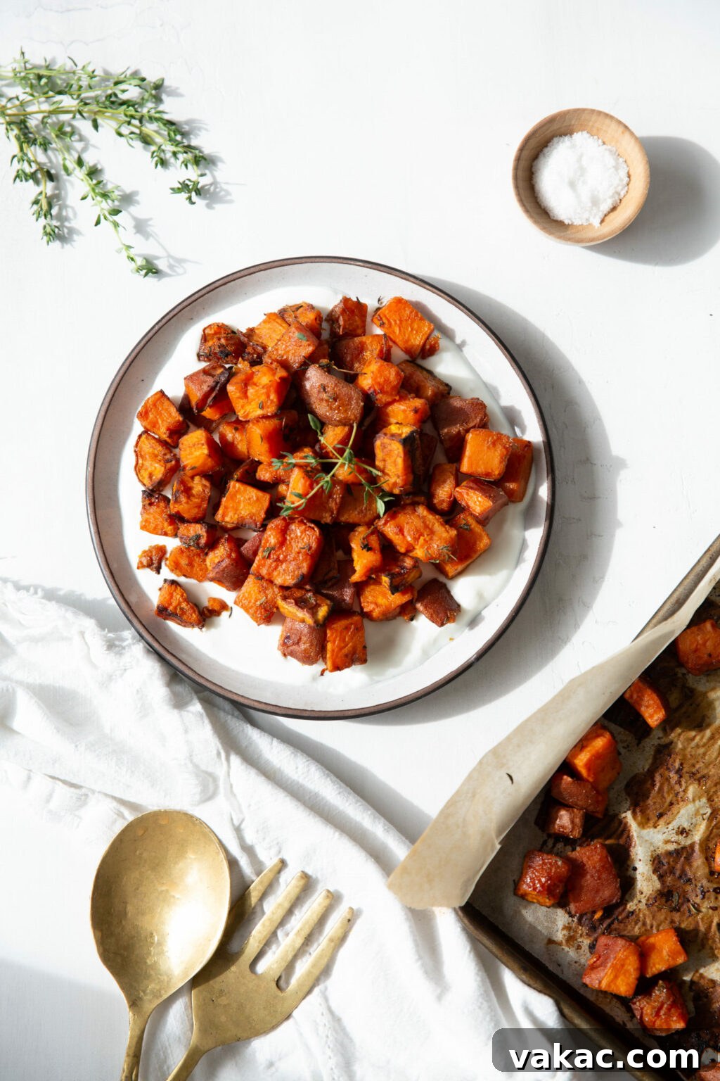 Irresistible Golden Sweet Potatoes with Velvety Garlic Aioli 2 A plate of oven baked sweet potatoes on top of a yogurt sauce. In the corner is a sprig of thyme and gold serving spoons.