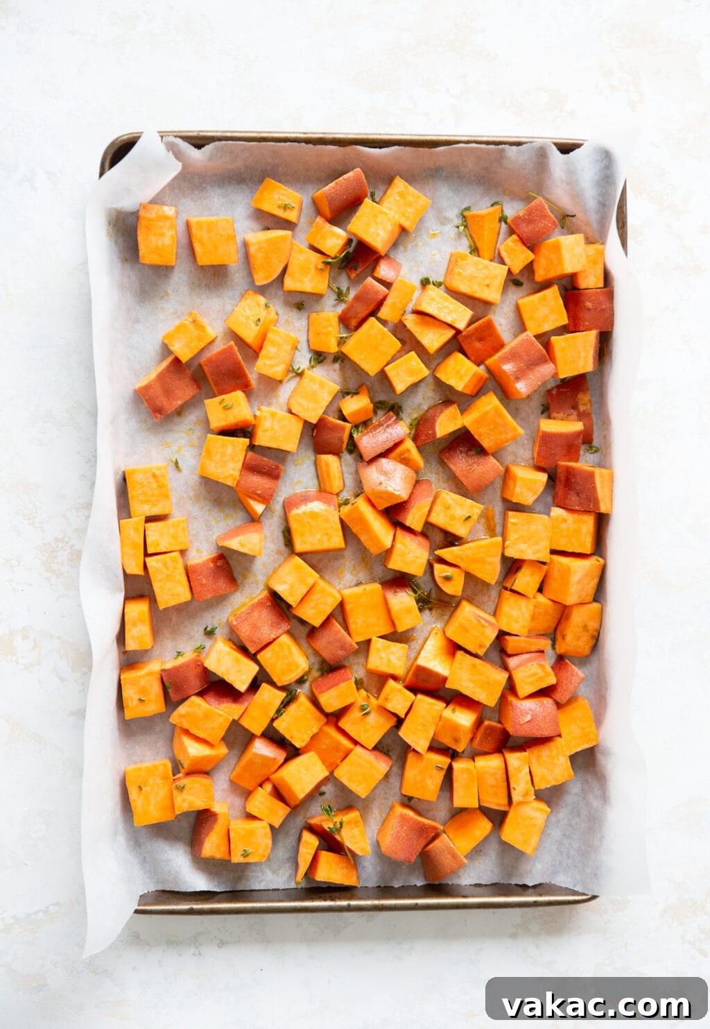 Irresistible Golden Sweet Potatoes with Velvety Garlic Aioli 3 Cubed sweet potatoes are on a baking sheet that is lined with parchment paper.