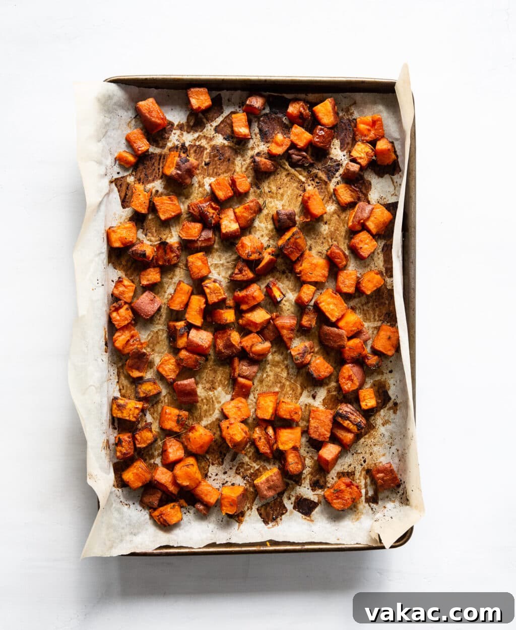 Irresistible Golden Sweet Potatoes with Velvety Garlic Aioli 4 A baking sheet lined with parchment paper has golden brown, baked sweet potatoes on it. The sweet potatoes are cubed.