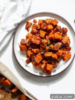 A plate of oven baked sweet potatoes on top of a yogurt sauce. In the corner is a sprig of thyme and gold serving spoons.