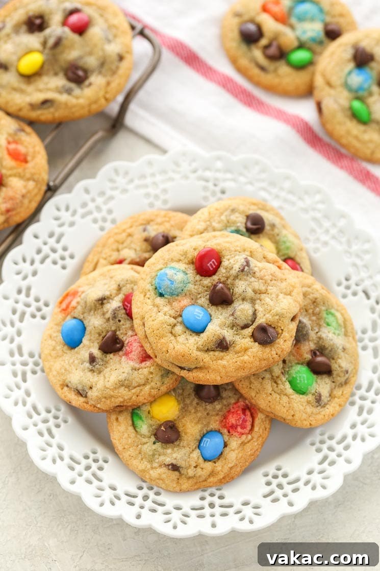 Ultimate Soft and Chewy M and M Chocolate Chip Cookies 2 A white plate piled high with chocolate chip M&M's cookies. Additional cookies rest in the background.