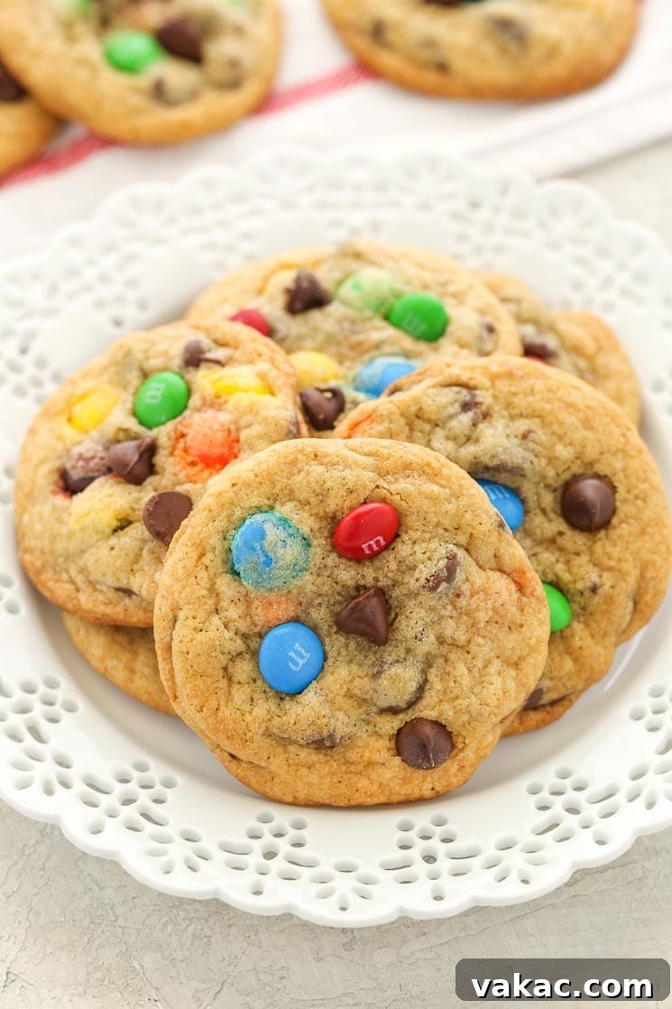 Ultimate Soft and Chewy M and M Chocolate Chip Cookies 4 A pile of M&M's cookies on a white plate. Additional cookies rest in the background.