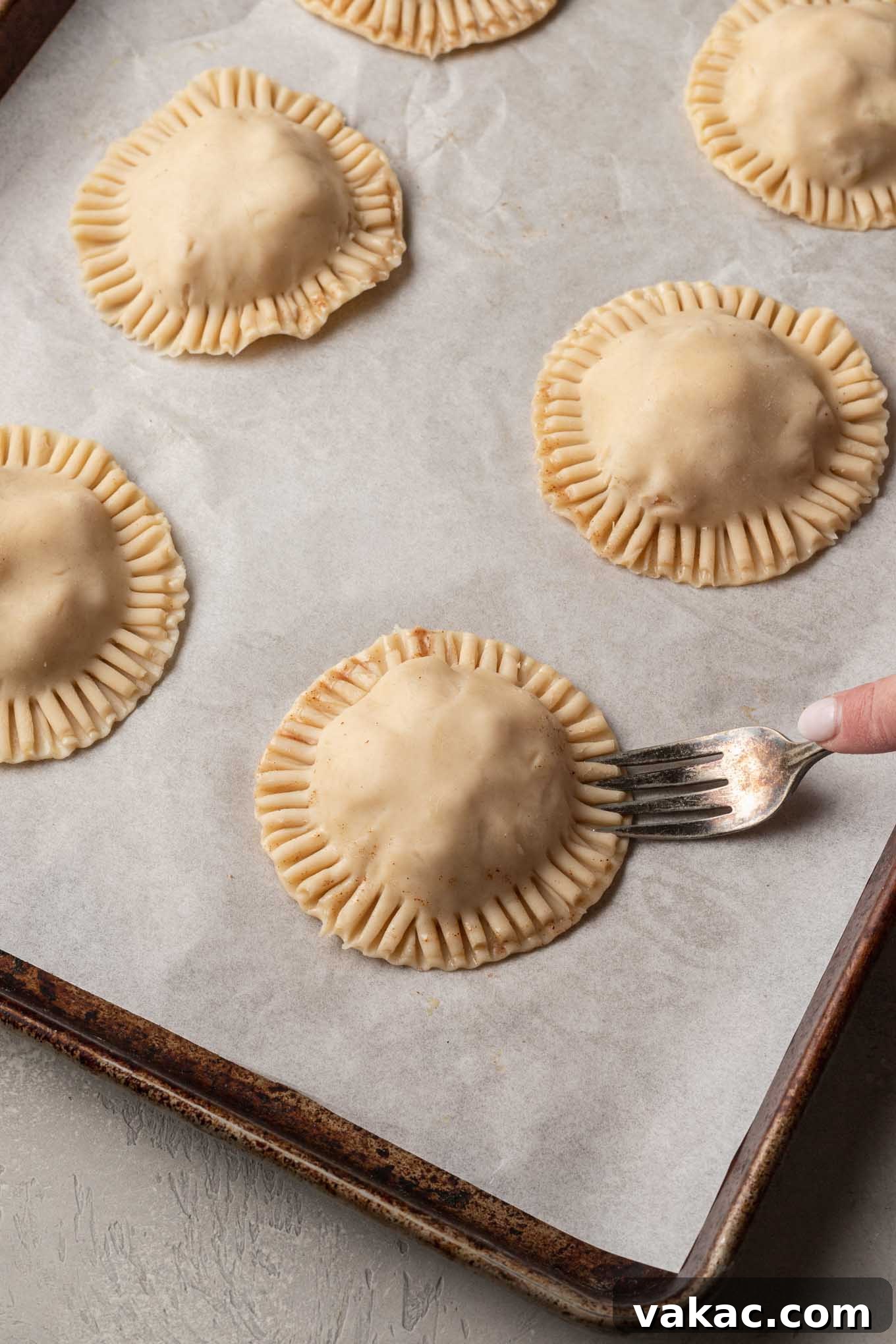 Golden Apple Pocket Pies 6 A process shot demonstrating the meticulous crimping of the edges of mini apple hand pies with a fork, ensuring a secure seal.