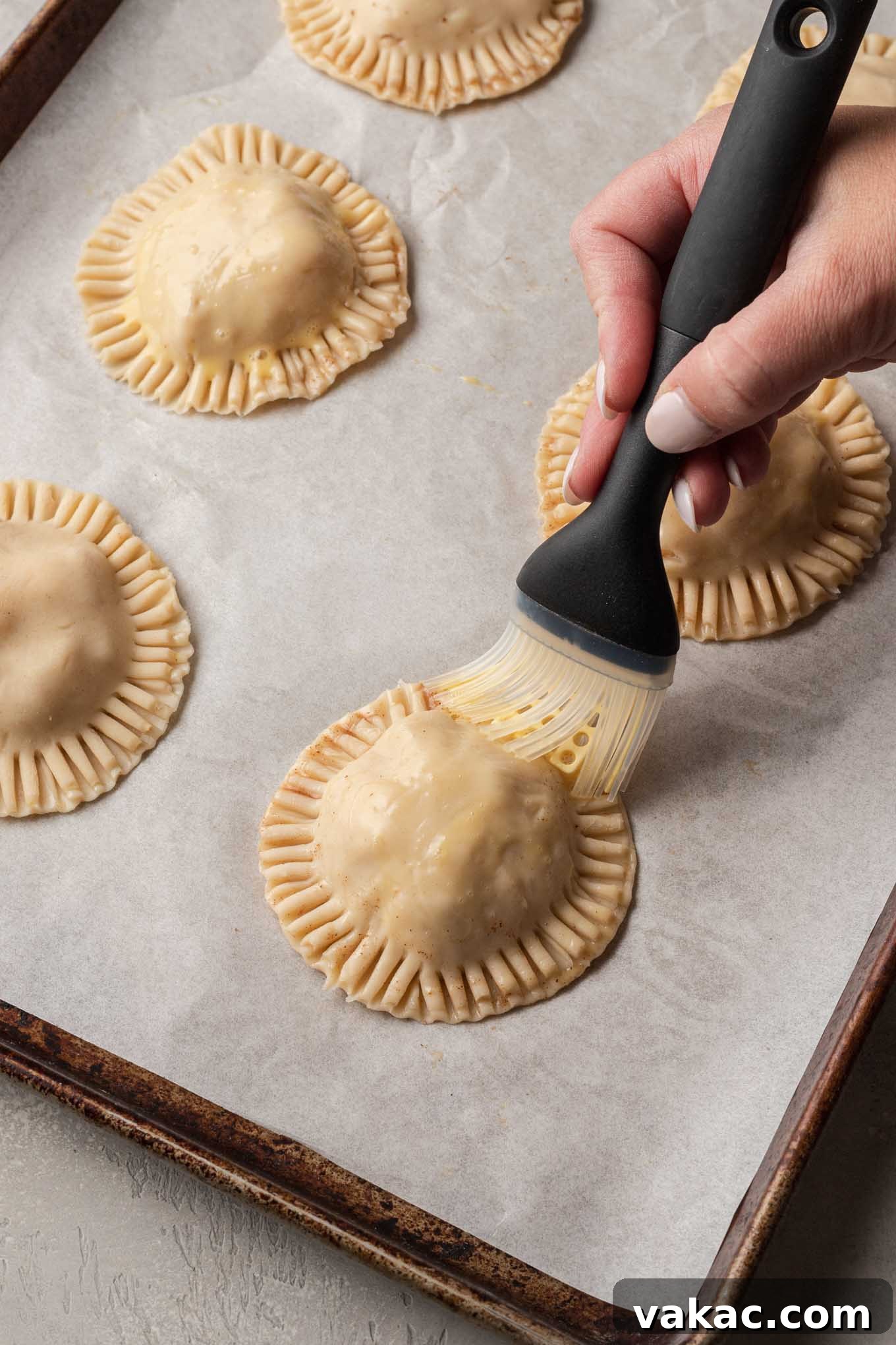 Golden Apple Pocket Pies 7 A process shot showing individual apple hand pies being carefully brushed with a golden egg wash, preparing them for a beautiful bake.