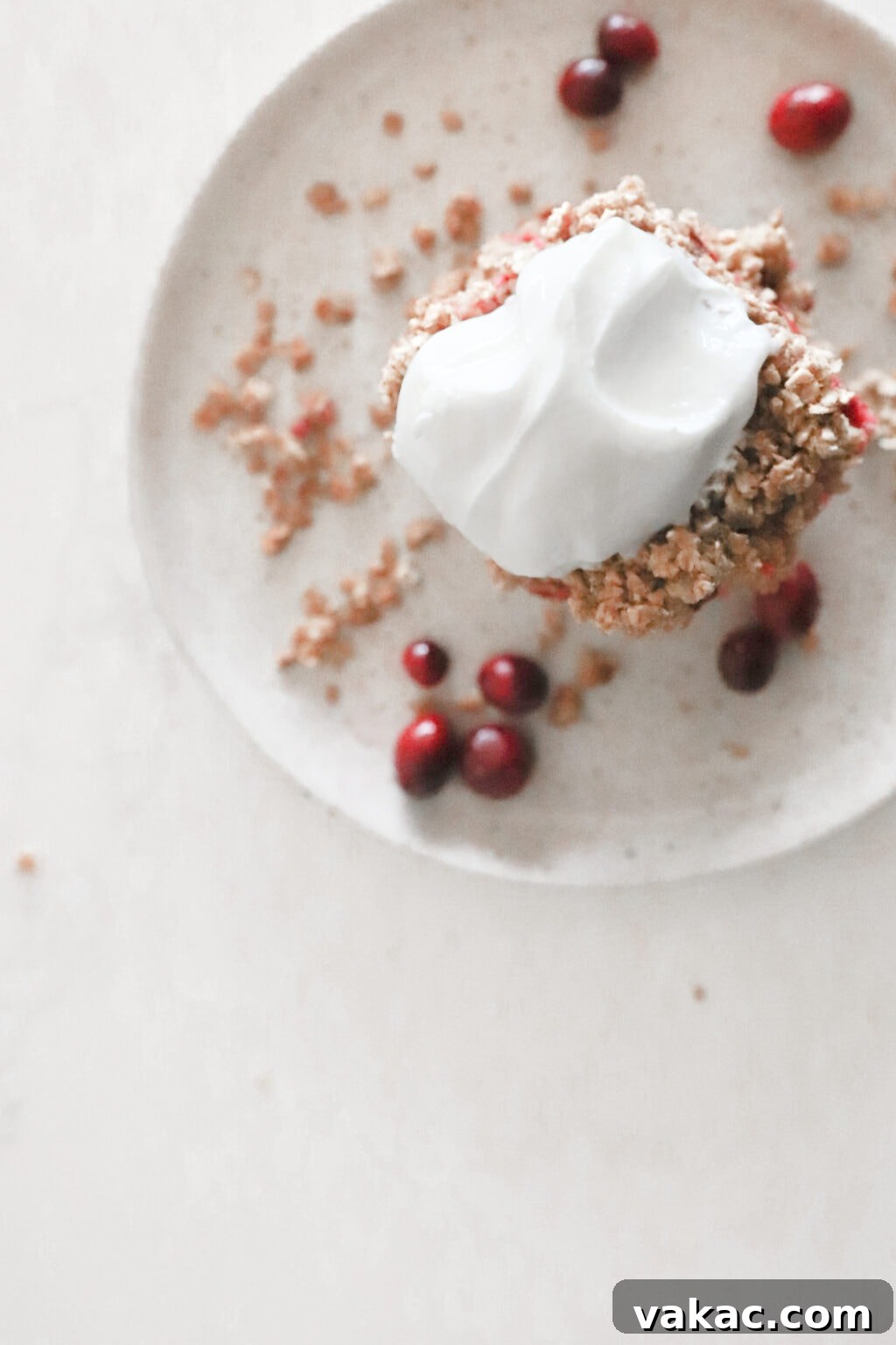 Chewy Cranberry Oat Bars 4 A grey plate has a cranberry oat bars stacked on top of each other and is topped with greek yogurt. The bars are surrounded by oat crumble and fresh cranberries.