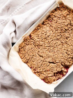 A 9 x 13 inch white baking dish contains baked cranberry oatmeal bars with cranberry sauce. The baking dish is surrounded by an off-white dish towel