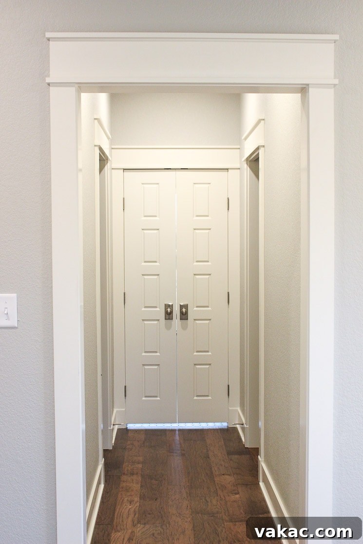 Our New Home Tour and Life Lately 17 An elegant hallway with walls painted in Sherwin Williams Repose Gray, featuring classic white craftsman trim and solid core doors, leading to a bathroom and hidden closet pocket doors.