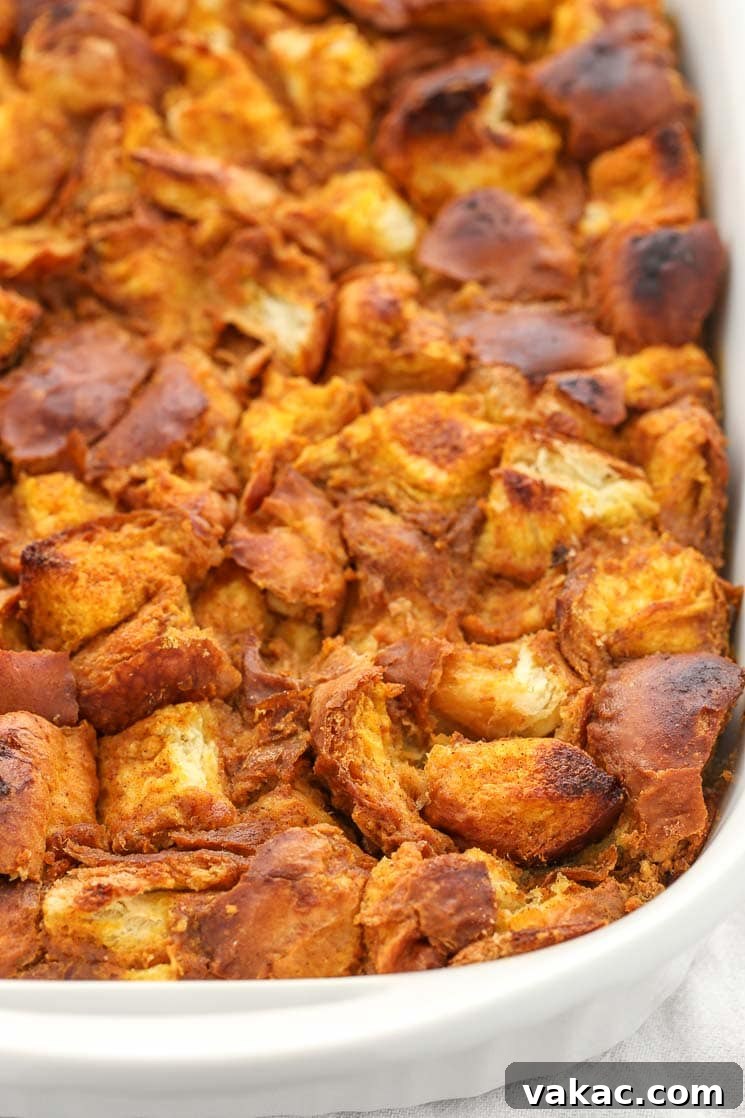 A beautiful white baking dish overflowing with golden-brown pumpkin bread pudding, fresh from the oven.