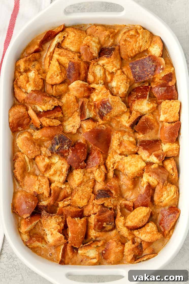 An overhead shot showcasing the unbaked pumpkin bread pudding in a white baking dish, with the bread fully soaked in the rich, spiced custard mixture, ready for the oven.