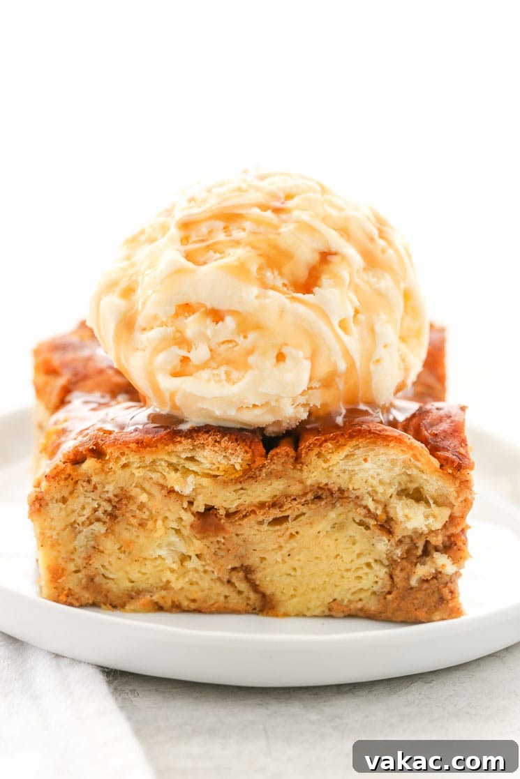 A perfectly portioned slice of warm pumpkin bread pudding, elegantly presented on a white plate, topped with a generous scoop of vanilla ice cream.