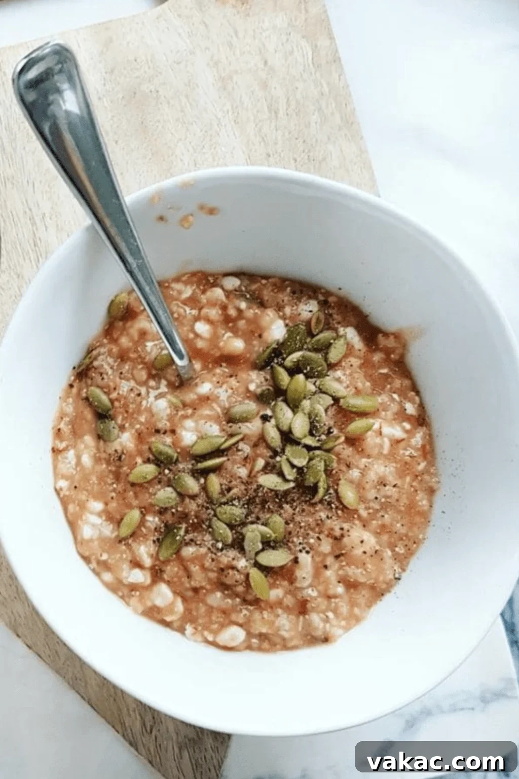 Savory Stovetop Pizza Oats 10 Minute Fix 2 A bowl of savory stovetop pizza oatmeal, garnished with vibrant pumpkin seeds and fresh herbs, rests on a rustic wooden board. A silver spoon is gently placed within the hearty oats, inviting a delightful first bite.