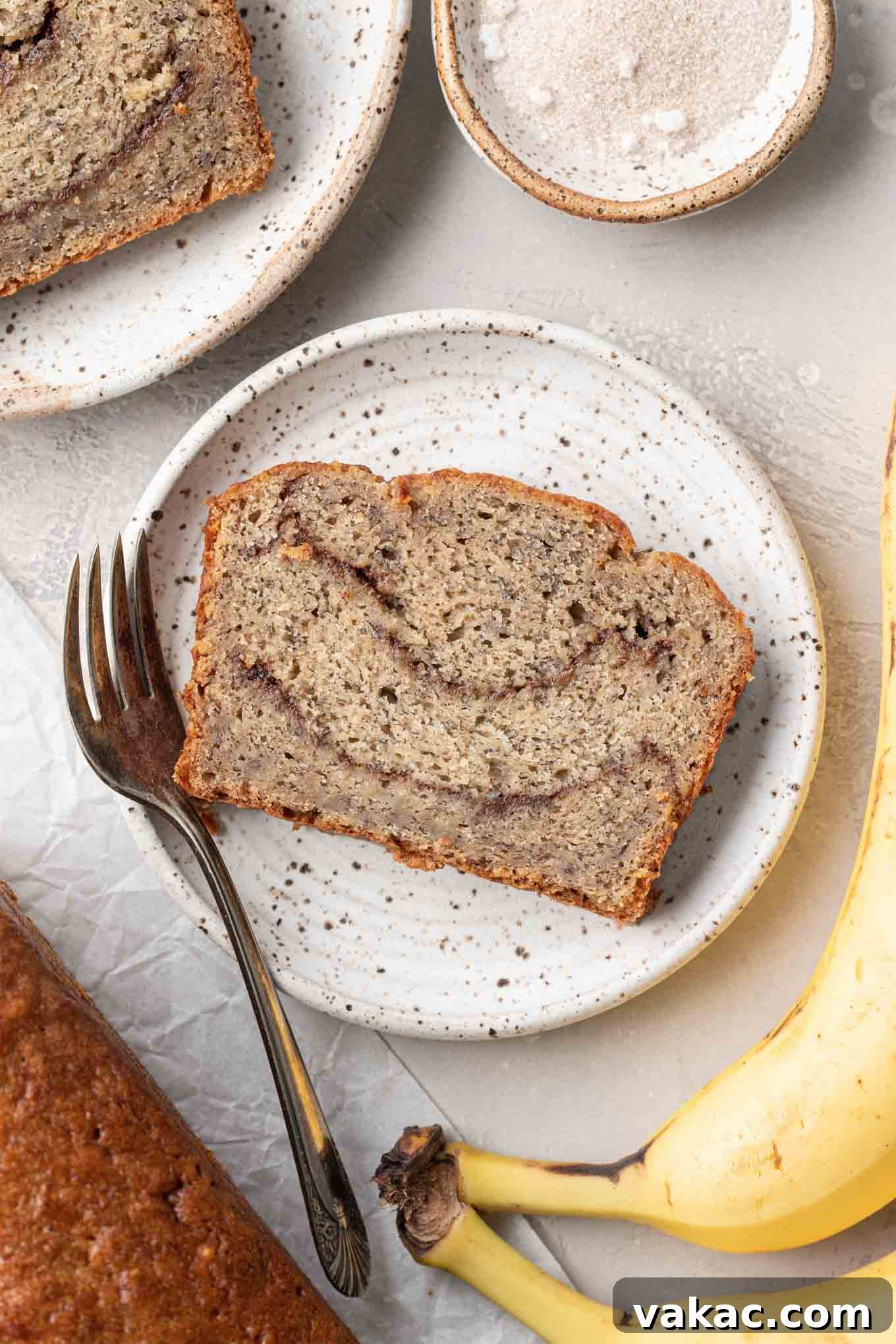 Marbled Cinnamon Banana Loaf 9 An overhead view of a perfectly sliced piece of banana cinnamon bread on a dessert plate, with a fork ready to enjoy.