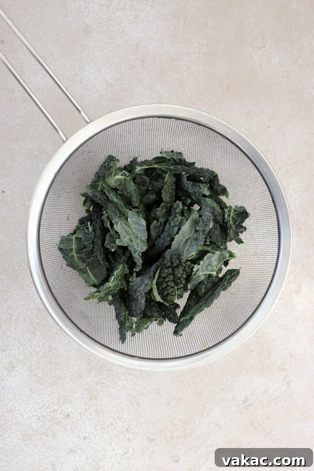 One bunch of fresh dino kale in a silver mesh strainer, ready for washing.