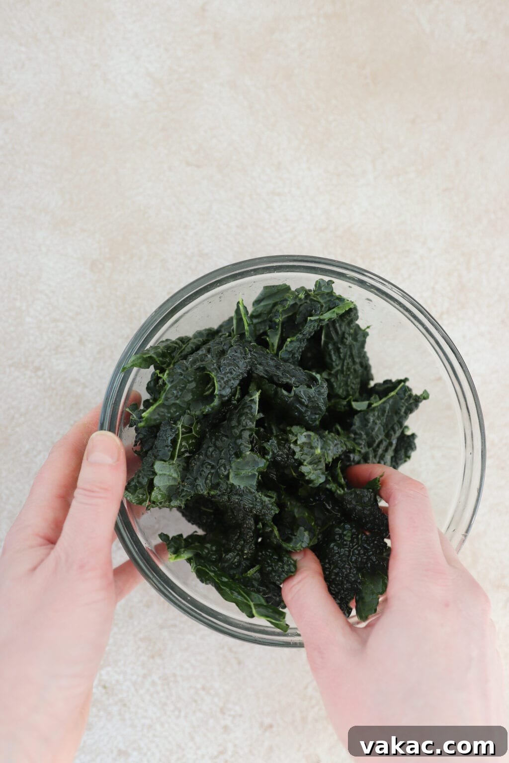 A hand gently massaging torn dino kale leaves in a clear bowl with olive oil or lemon juice.
